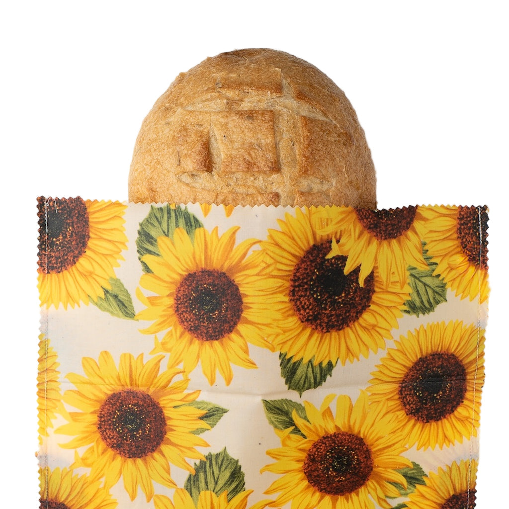 Sunflower-patterned beeswax wrap with a loaf of bread inside on a white background